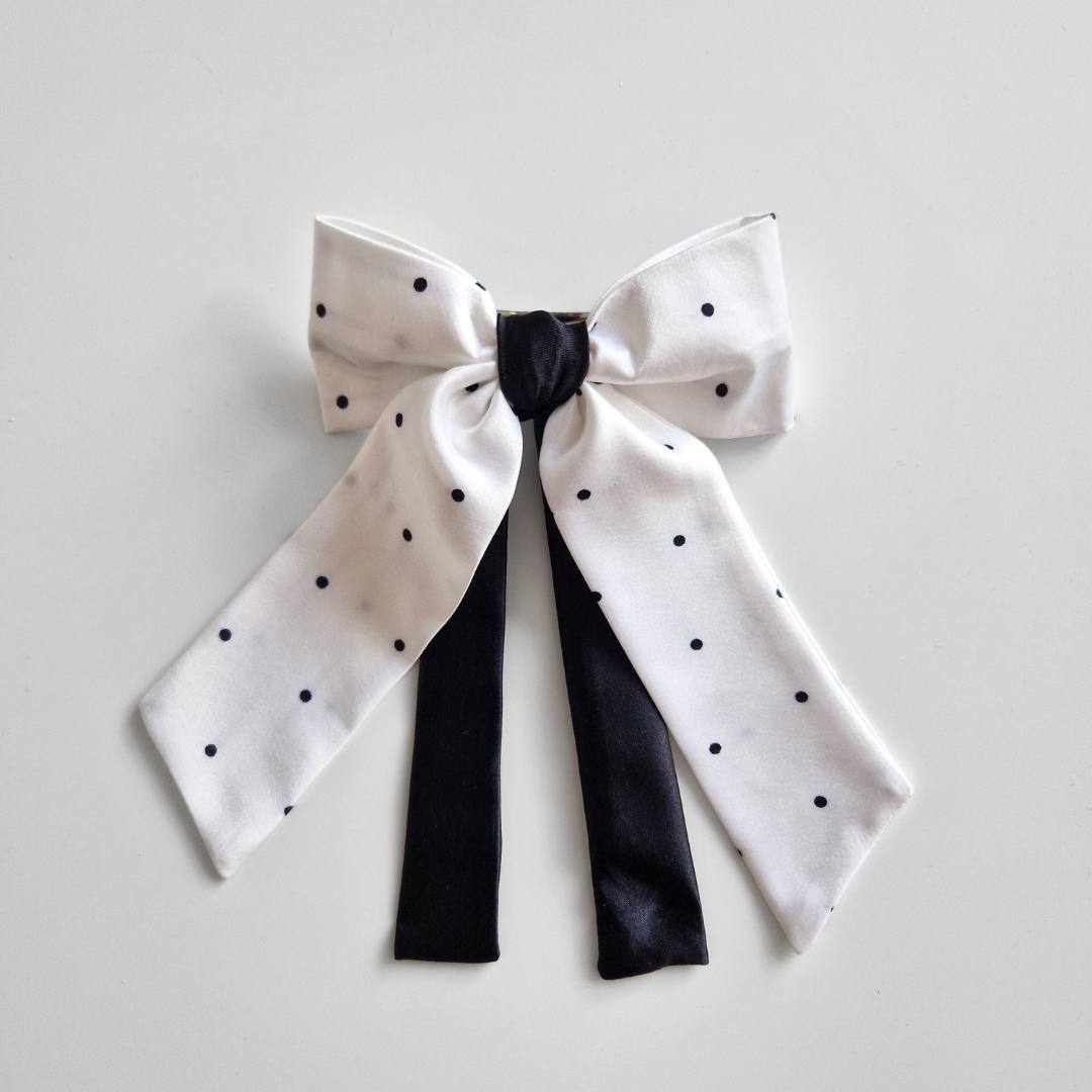 White bow with black polka dots and black ribbon on a light gray background