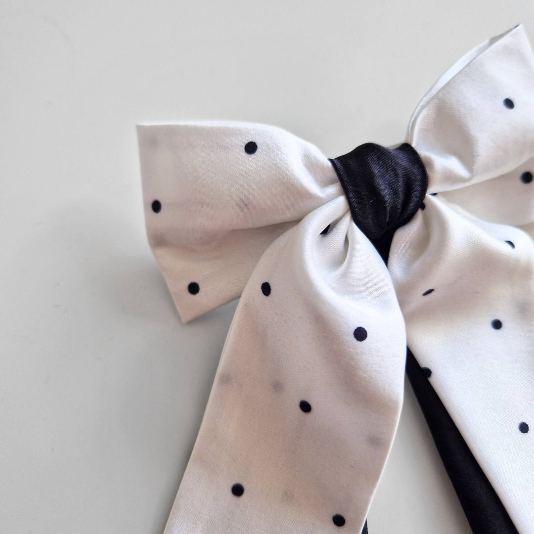 White bow with black polka dots on a light gray background
