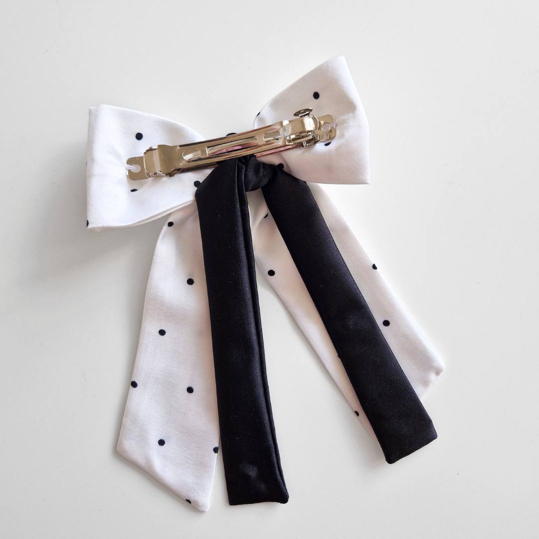 White polka dot bow hair clip with black ribbons on a light gray background