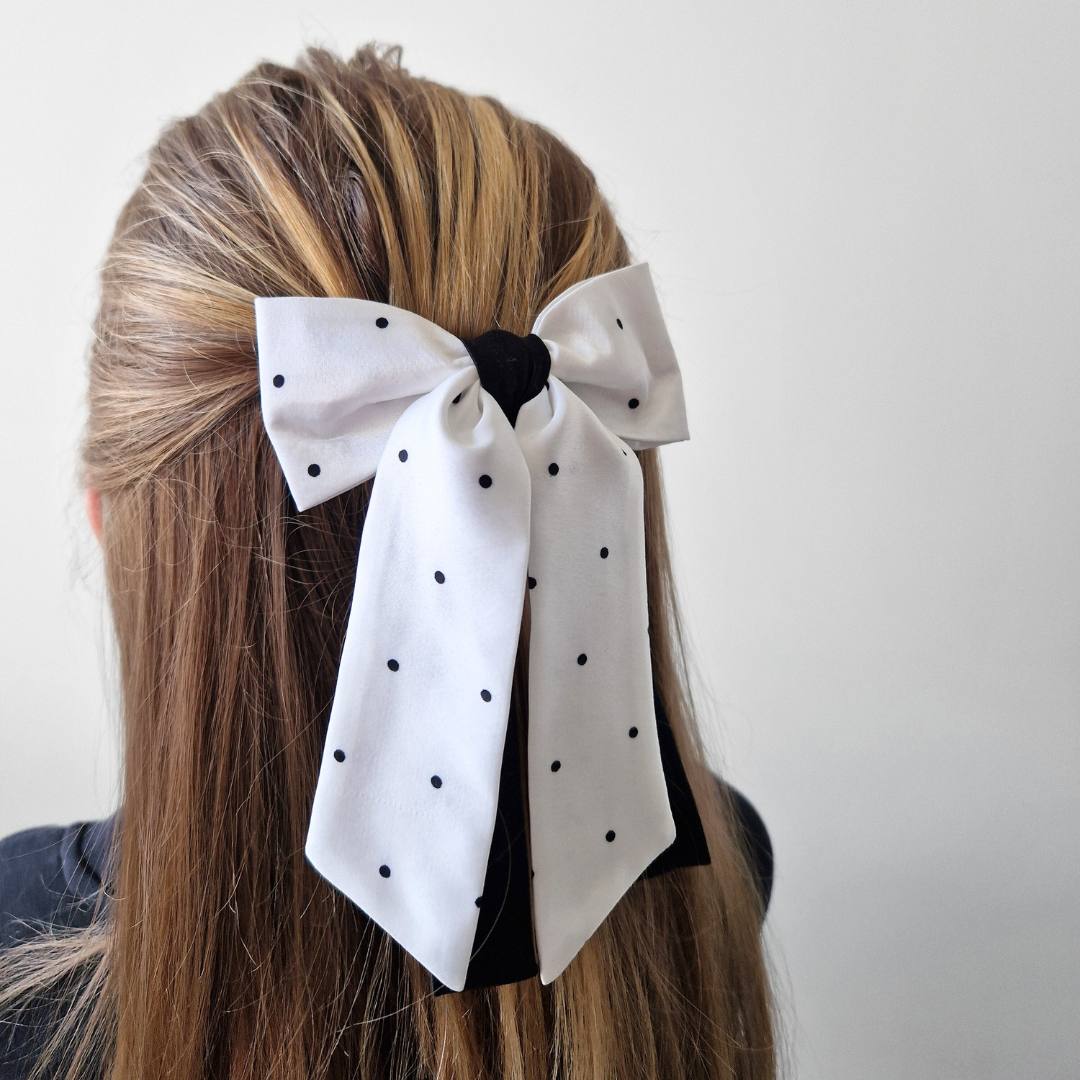 White polka dot hair bow in a person's hair against a plain background