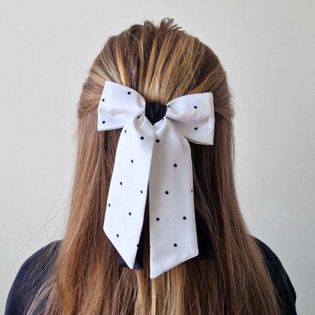 White polka dot hair bow in a person's hair against a plain background