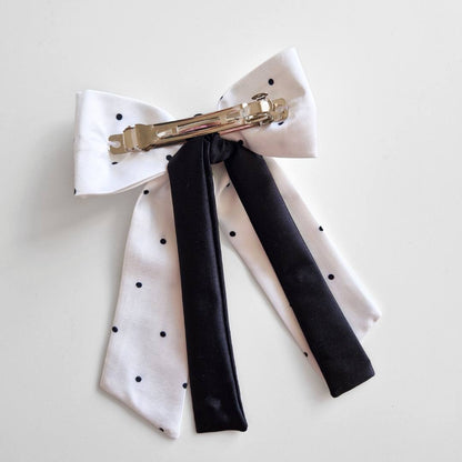 White polka dot bow hair clip with black ribbons on a light gray background