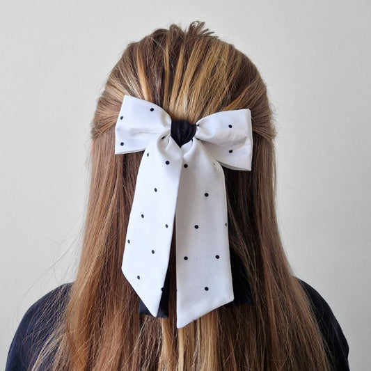 White polka dot hair bow in a person's hair against a plain background