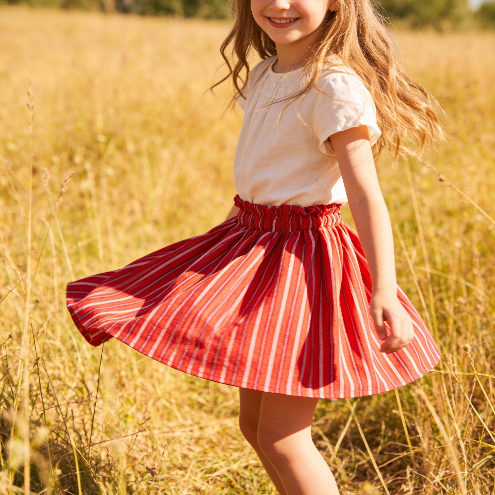Young girl in a red and white striped skirt standing in a field of tall grass.