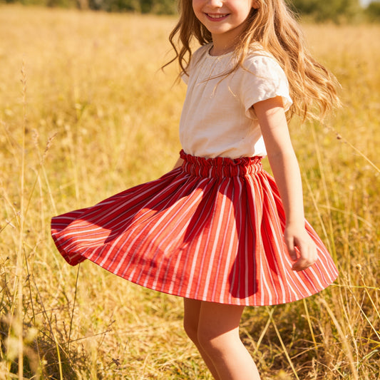 Young girl in a red and white striped skirt standing in a field of tall grass.